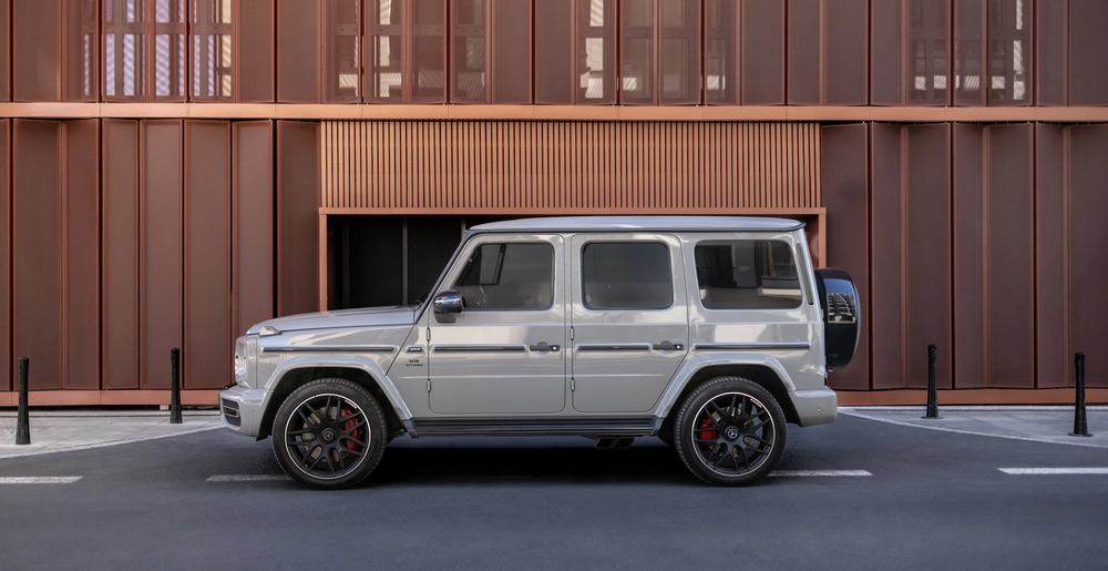 Mercedes-AMG G63 на фоне современного здания: мощный внедорожник с характерным дизайном, выразительными дисками и агрессивным стилем, сочетающий роскошь и проходимость.