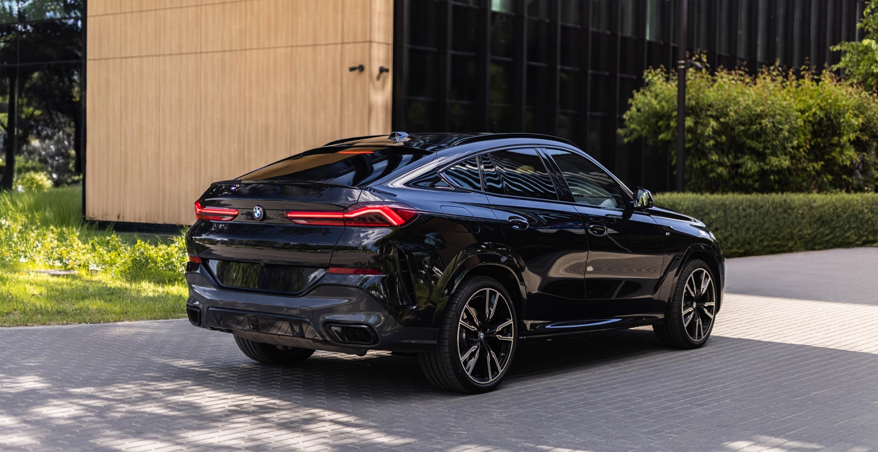 Czarny BMW X6 xDrive40d M Sport – widok z tyłu i z boku na tle nowoczesnego budynku. Auto dostępne w SK CARS Warszawa.