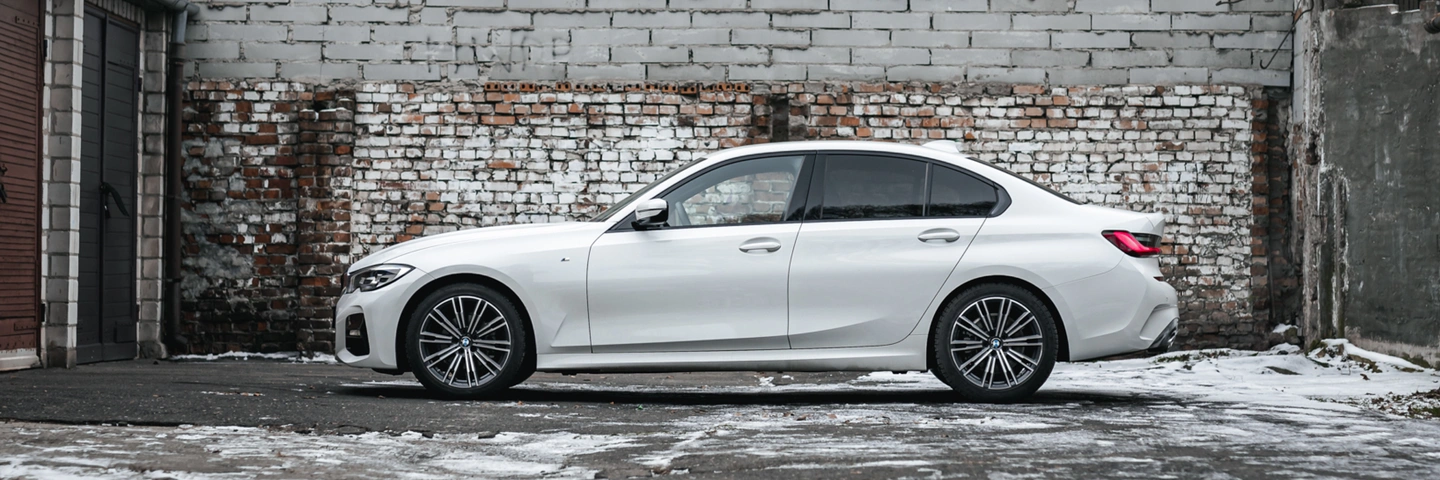 A white BMW 3 Series against a rustic brick wall backdrop. A stylish and comfortable car available for rent at SK CARS.