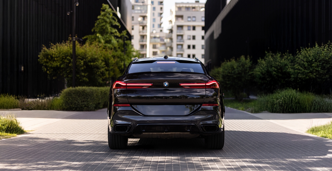 Tył BMW X6 – światła LED, sportowy dyfuzor i podwójny wydech. Samochód zaparkowany między nowoczesną zabudową.