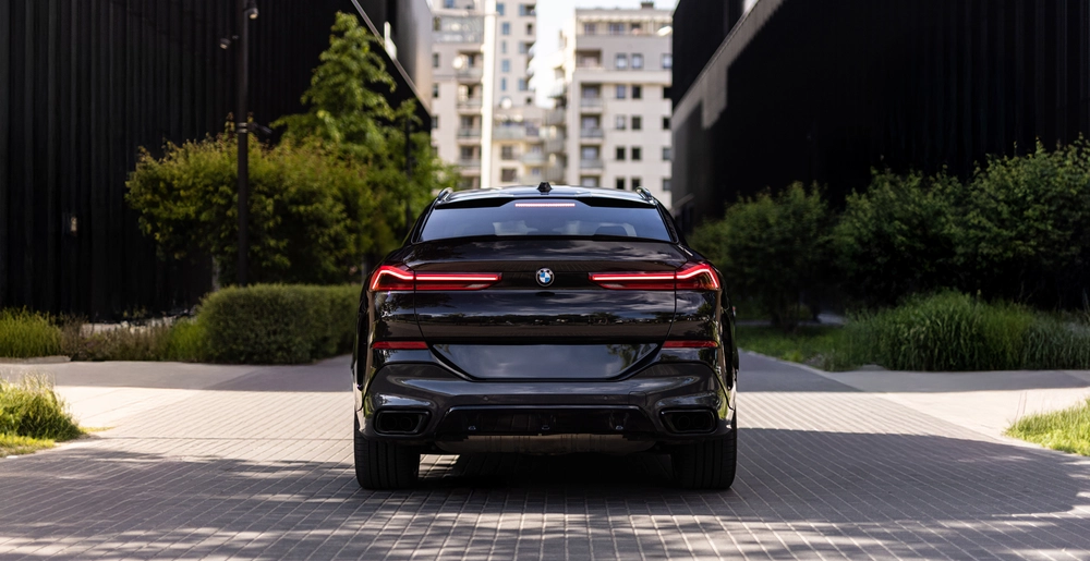 Tył BMW X6 – światła LED, sportowy dyfuzor i podwójny wydech. Samochód zaparkowany między nowoczesną zabudową.