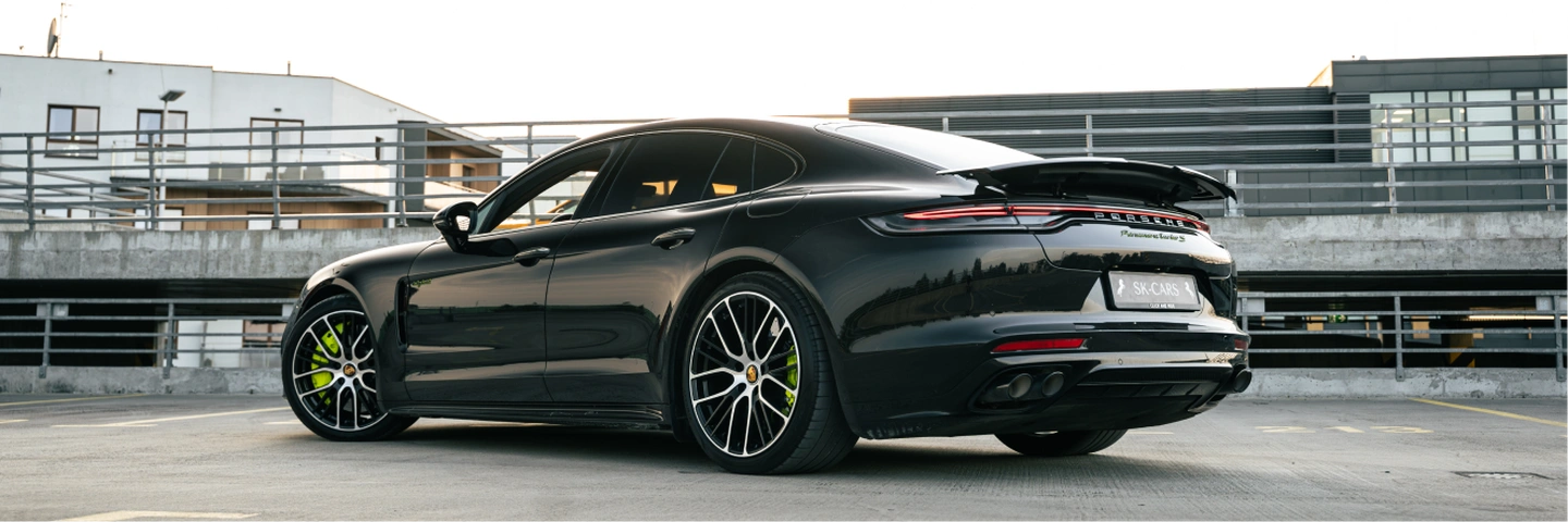 Black Porsche Panamera Turbo S E-Hybrid on a rooftop parking in Warsaw, rear three-quarter view.