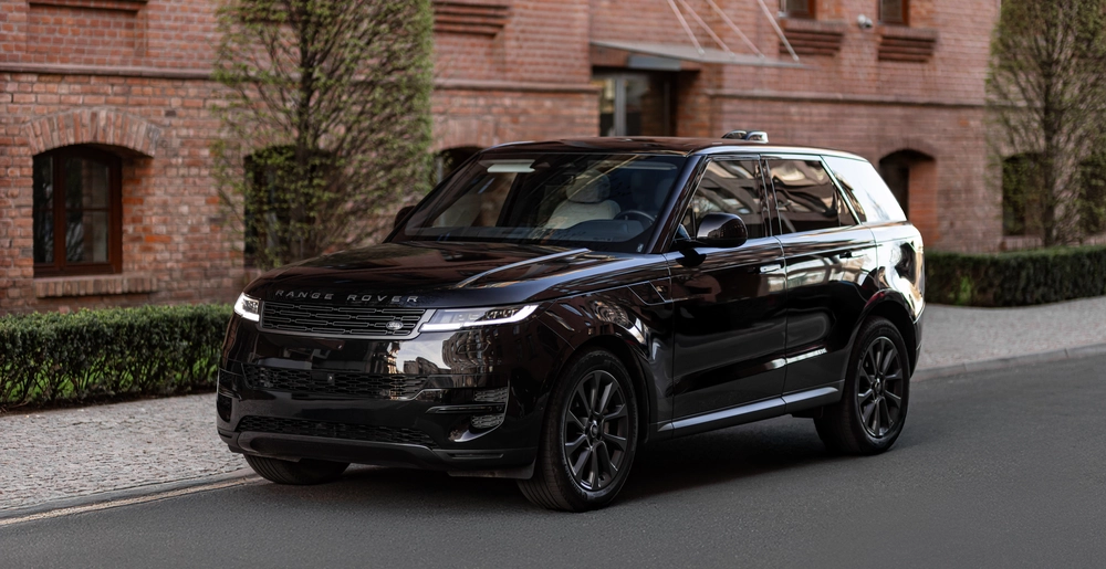 Czarny Range Rover Sport zaparkowany na tle ceglanego budynku i zieleni.