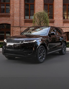 Czarny Range Rover Sport zaparkowany na tle ceglanego budynku i zieleni.