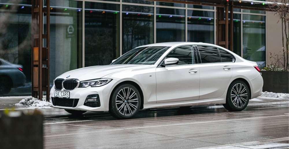 Biały BMW 3 Series przed nowoczesnym budynkiem. Elegancki sedan do wynajmu w SK CARS dla wygodnych podróży w mieście i poza nim.