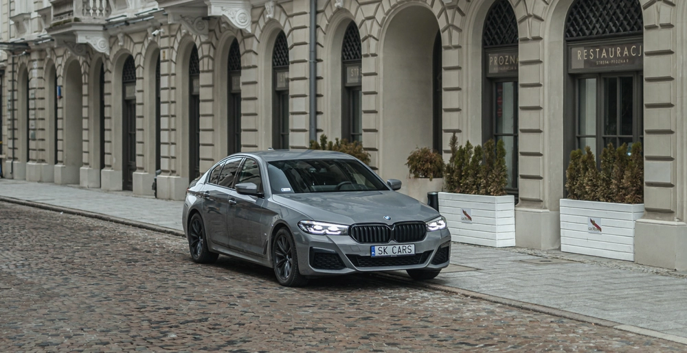 BMW 5 серии серого цвета на исторической улице города. Элегантность и комфорт, доступные для аренды в SK CARS.